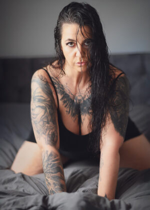 Erotikmodel Mara LeNoir mit nassem Haar auf dem Bett – Tattoos und Blick im Fokus