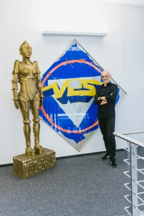 CEO Andreas Kirchen steht neben einer goldenen Metropolis-Skulptur vor einem großen VPS-Logo-Kunstwerk im Firmengebäude von VPS Film.