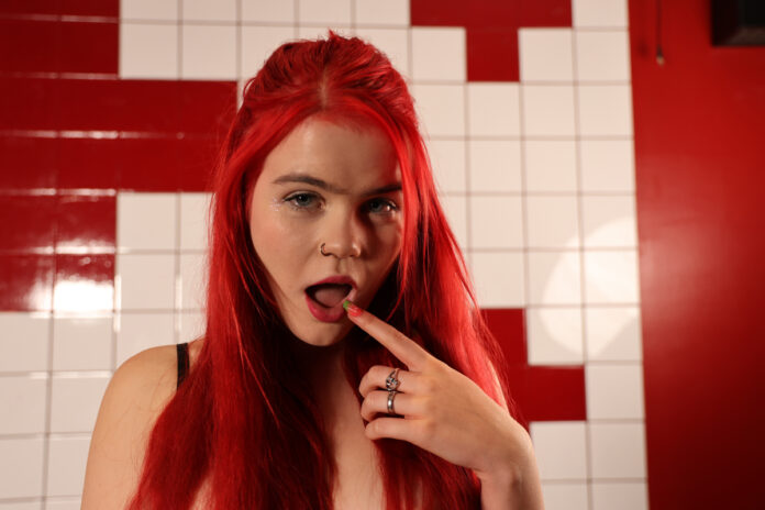 Mia May: GAN Girl des Monats (Februar 2026) Mia May mit intensivem Blick und rotem Hintergrund im Editorial-Shooting