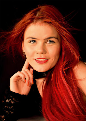 Mia May: GAN Girl des Monats (Februar 2026) Porträt von Mia May mit leuchtend rotem Haar vor schwarzem Hintergrund beim Studio-Shooting