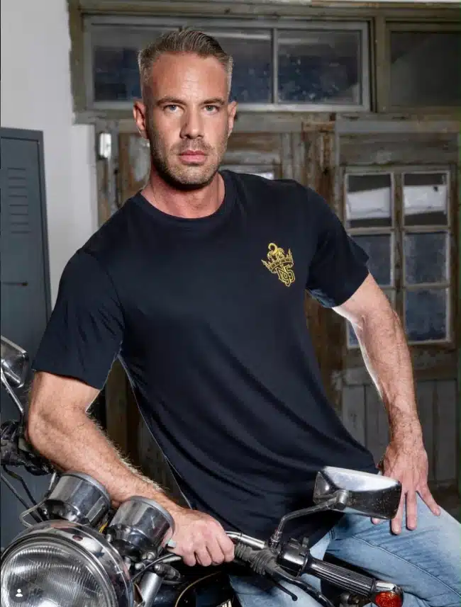Chris Gun im schwarzen N95-Shirt mit goldenem Brustmotiv an einem Motorrad.