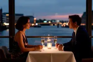 Elegant gekleidetes Paar beim Dinner bei Kerzenlicht an einem Fensterplatz mit Blick auf das abendliche Hamburger Hafenwasser